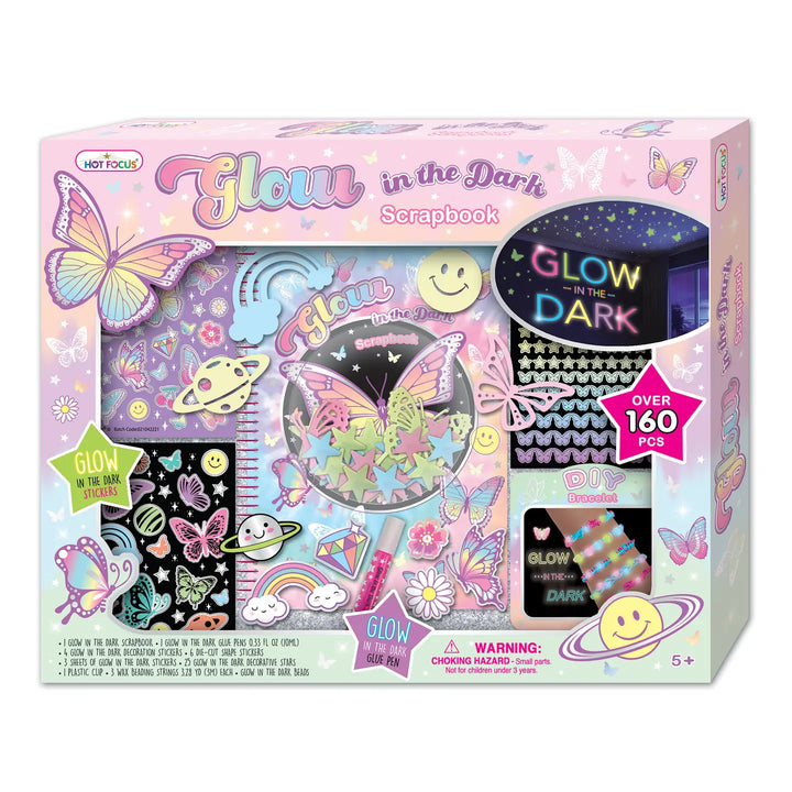 Packaging for Glow in the Dark Scrapbook kit, featuring a pink box with illustrations of butterflies, planets, and stars, and a sneak peek window displaying the glow-in-the-dark components.