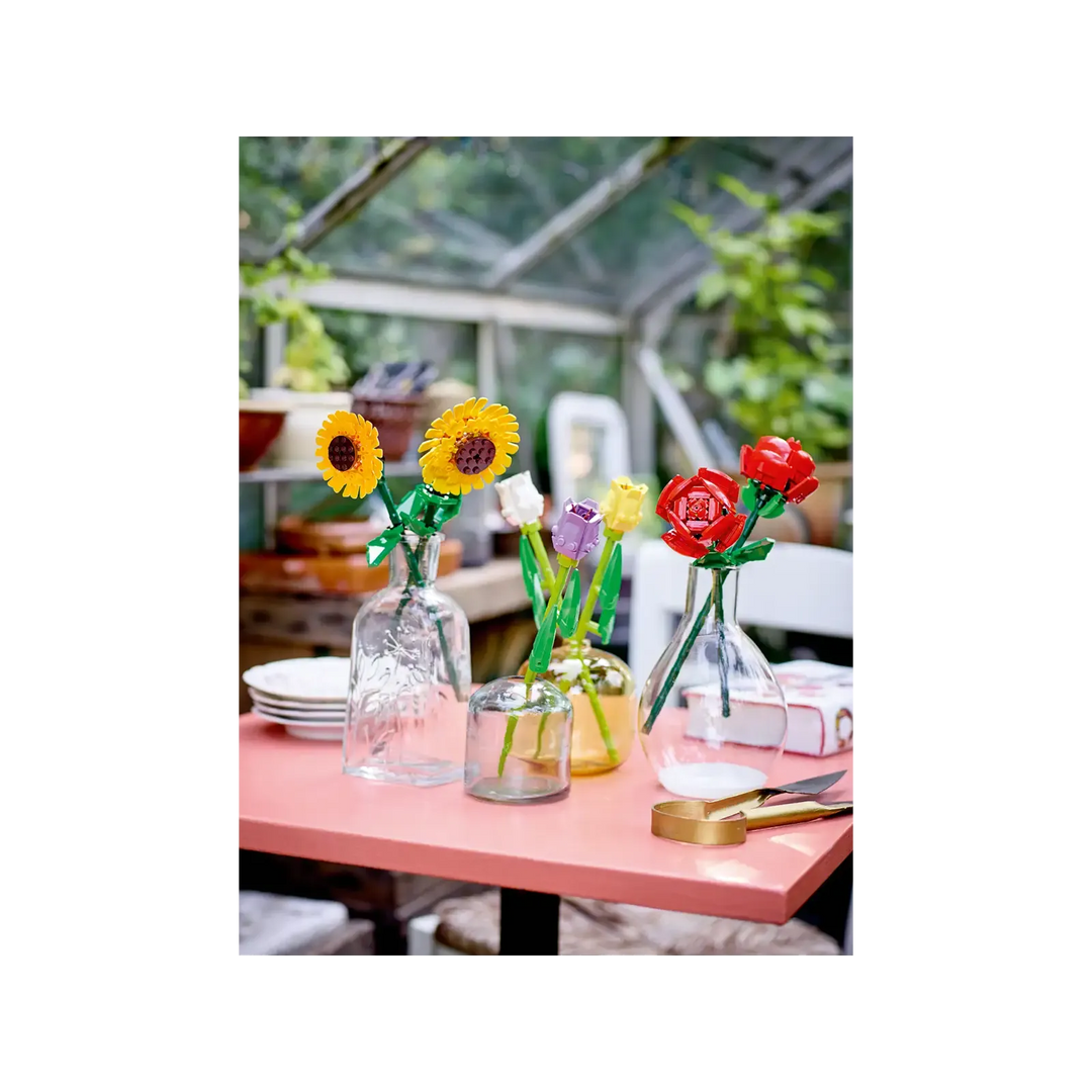 Colorful flower arrangements in glass vases on a table with a greenhouse background
