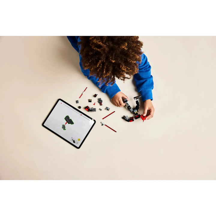 Child playing with building blocks on a beige surface with a tablet displaying a similar activity.