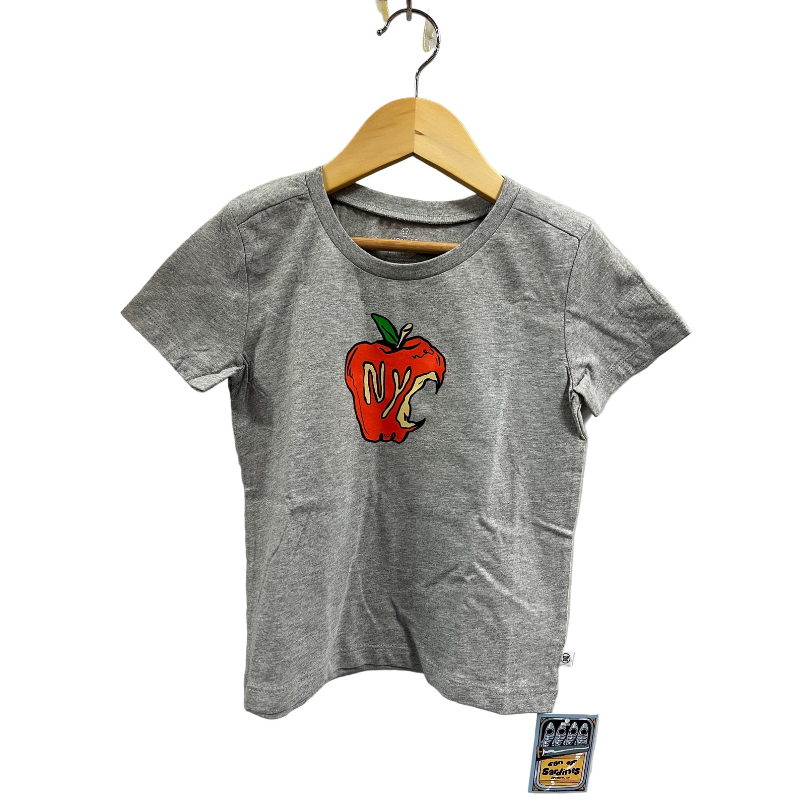 Gray t-shirt with a red apple graphic on a hanger against a white wall.