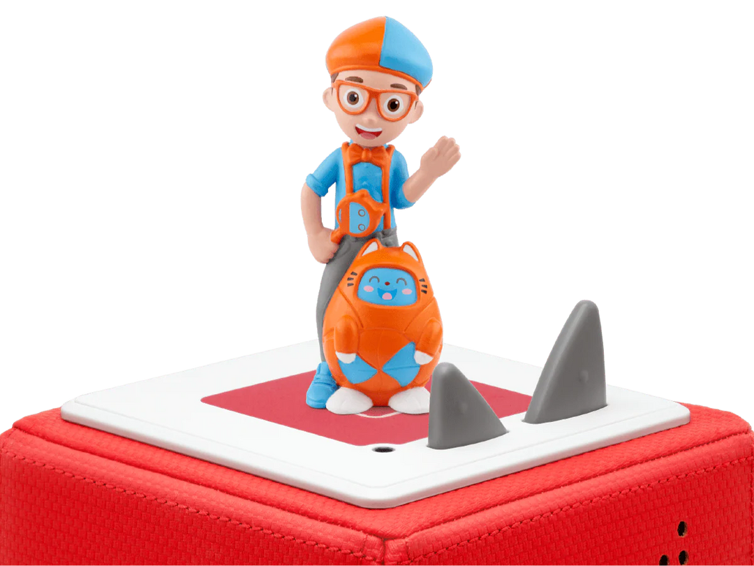 Toy figure of a character with a blue hat and orange outfit, standing on a red and white toy shark.