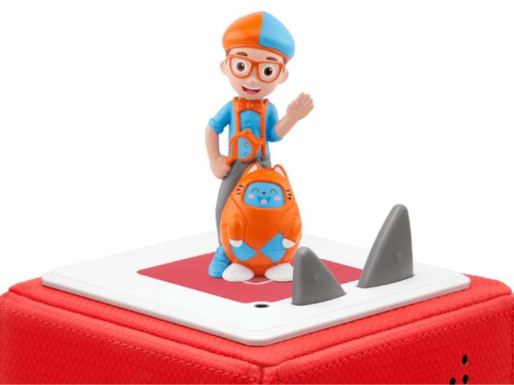 Toy figure of a character with a blue hat and orange outfit, standing on a red and white toy shark.