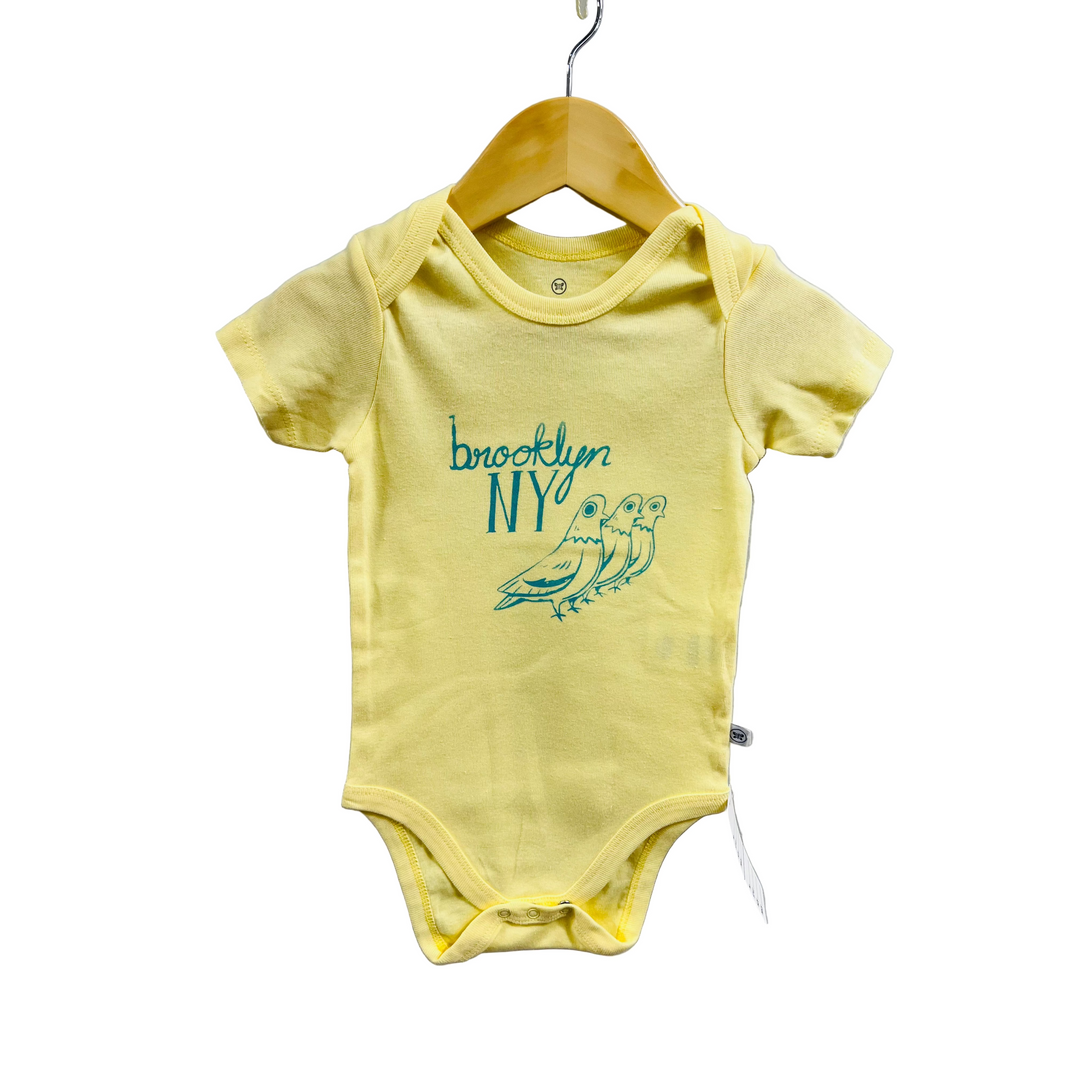 Yellow baby onesie with 'Brooklyn NY' and bird design on a hanger against a white background