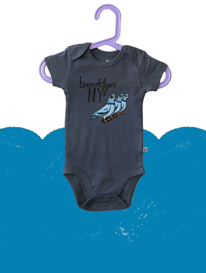 Gray baby onesie with 'Brooklyn NY' design on a purple hanger against a blue background