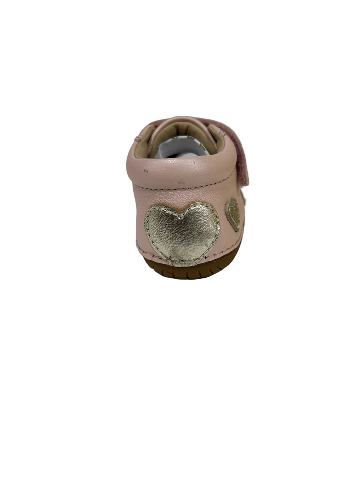 A single baby bootie in light pink leather, shown from the back. It features a metallic silver heart applique on the back and a brown rubber sole, resting on a white surface.