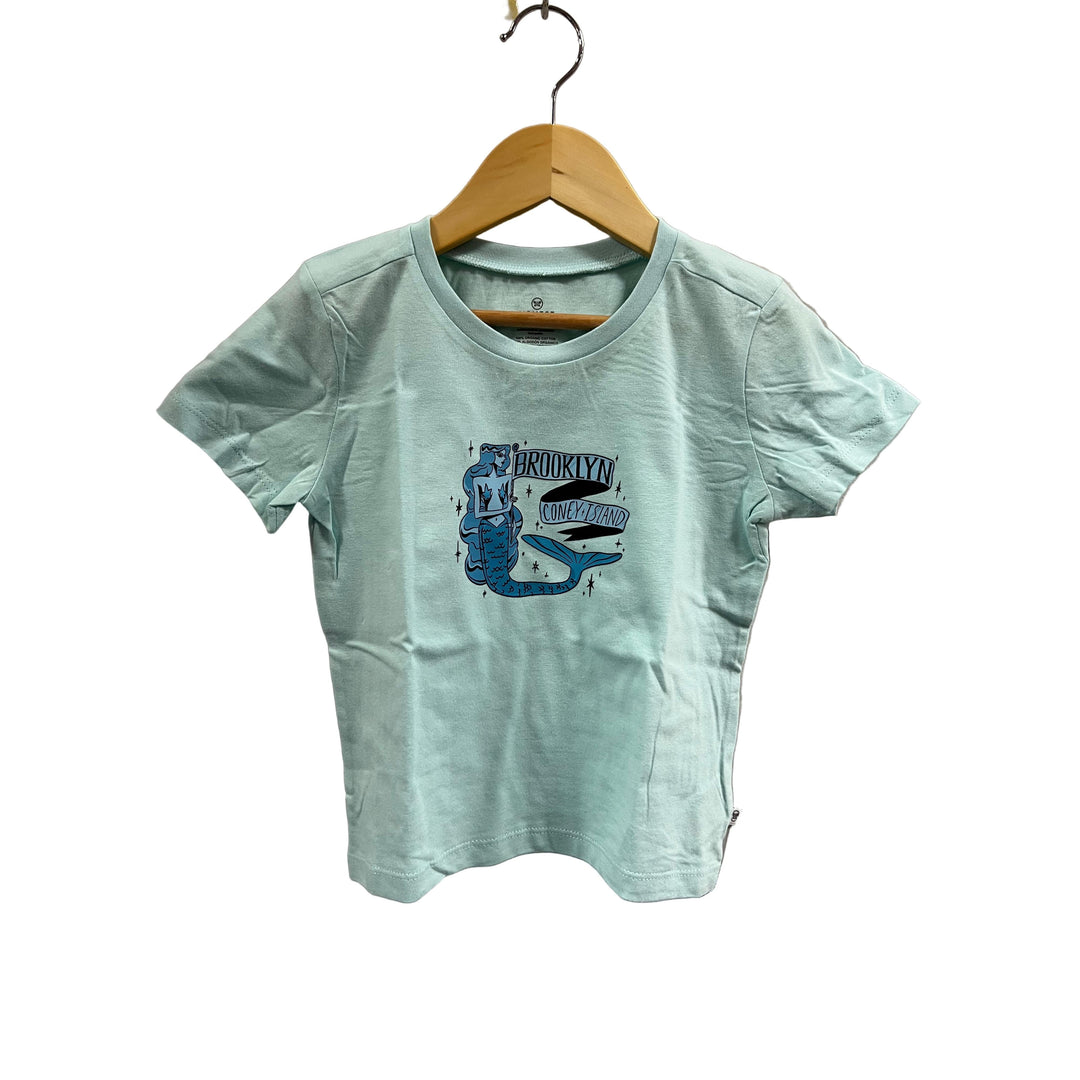 Light blue t-shirt with a graphic design on a wooden hanger against a beige wall.