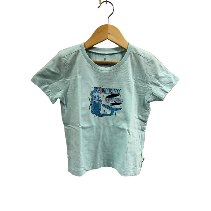 Light blue t-shirt with a graphic design on a wooden hanger against a beige wall.