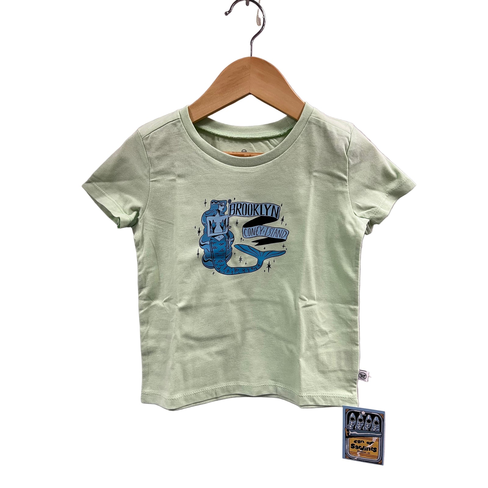 Light green t-shirt with blue graphic design on a hanger against a purple background