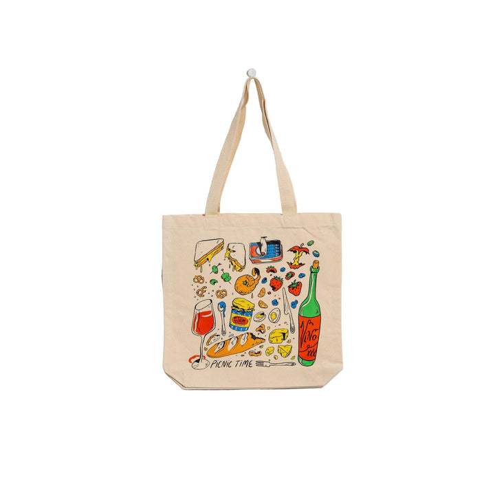 Beige tote bag with colorful picnic-themed illustrations on a light gray background