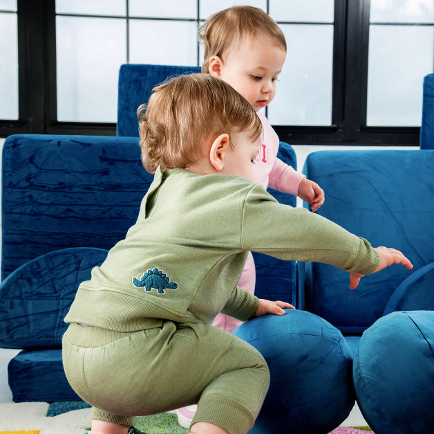 Two children playing on a blue couch with a dinosaur-themed outfit.