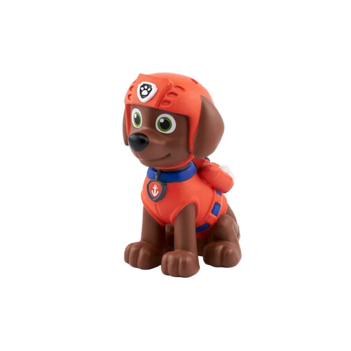 A plastic figure of PAW Patrol character Zuma the dog, dressed in his orange and blue uniform, sitting against a white background.