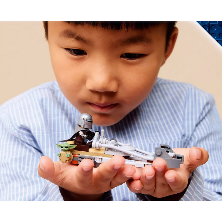 A young boy in a blue and white striped shirt holds a small LEGO Star Wars build in his hands, looking closely at it.