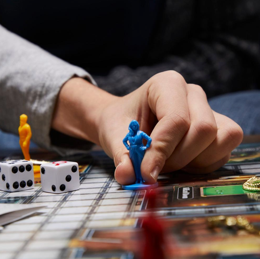 Hand placing a blue figurine on a board game with dice and other pieces.