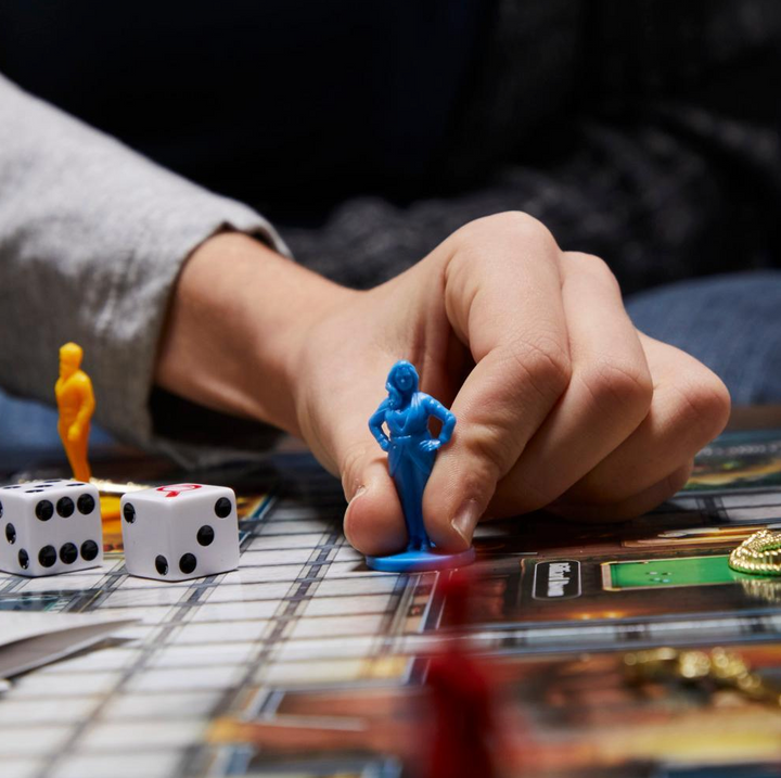 Hand placing a blue figurine on a board game with dice and other pieces.