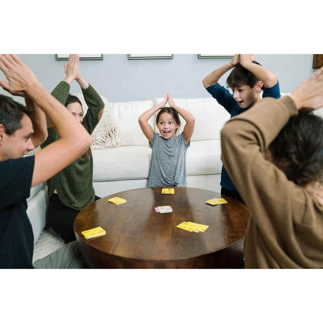 Children and adults playing a game with cards on a table in a living room.