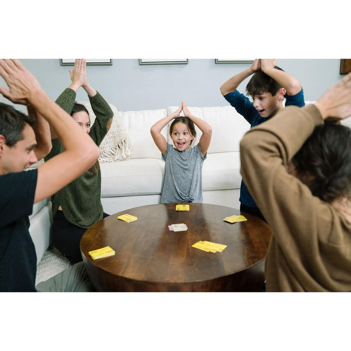 Children and adults playing a game with cards on a table in a living room.