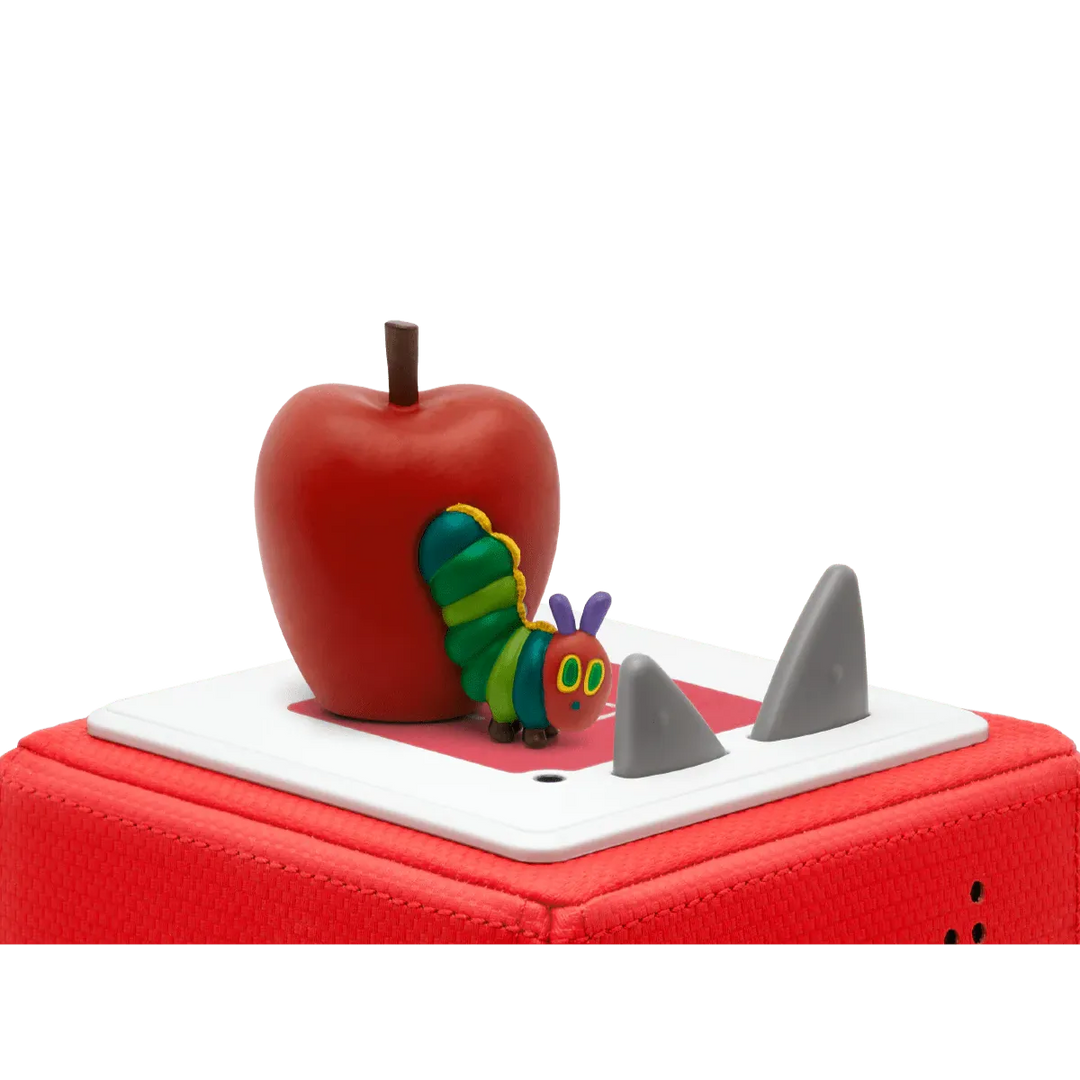Red apple with a colorful caterpillar toy on top of a red suitcase.