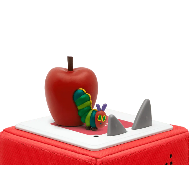 Red apple with a colorful caterpillar toy on top of a red suitcase.