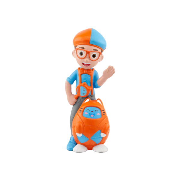 A figurine of the character Blippi from the children's series, standing with a smile, wearing a blue and orange outfit, gray pants, and blue hat and glasses. He is holding a blue backpack and there is a gray cat inside the backpack.