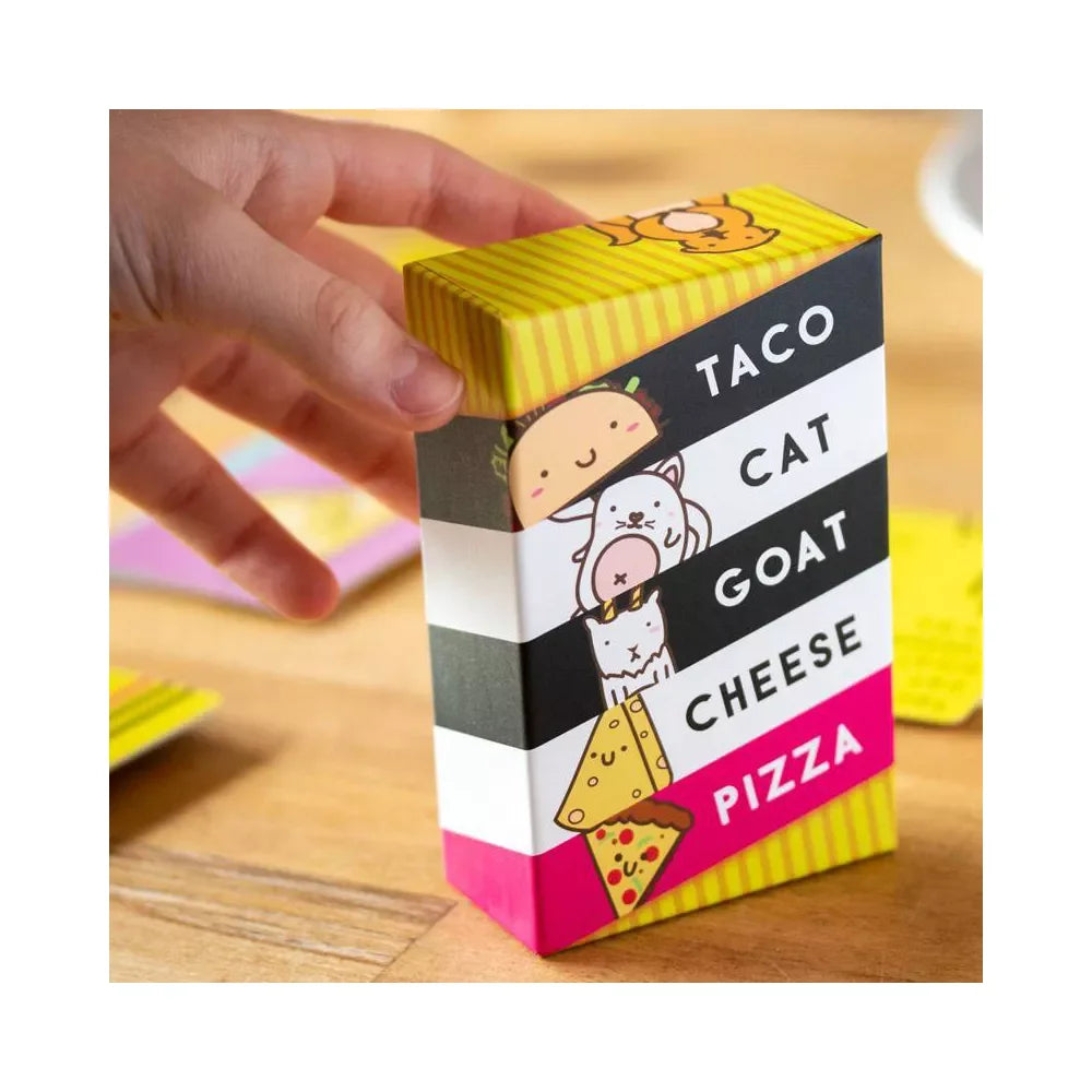 Colorful box labeled 'Taco Cat Goat Cheese Pizza' with cartoon illustrations on a wooden surface.