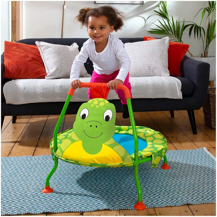 Child playing with a green turtle-shaped trampoline in a living room.