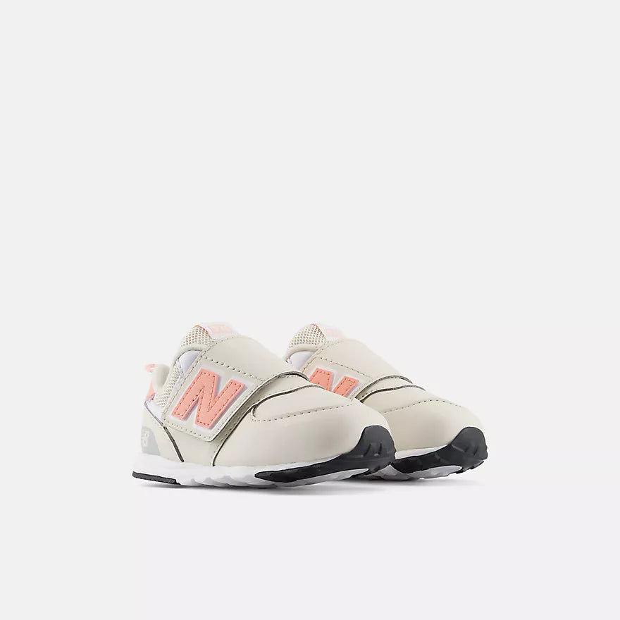 A pair of New Balance toddler sneakers in off-white with coral pink &